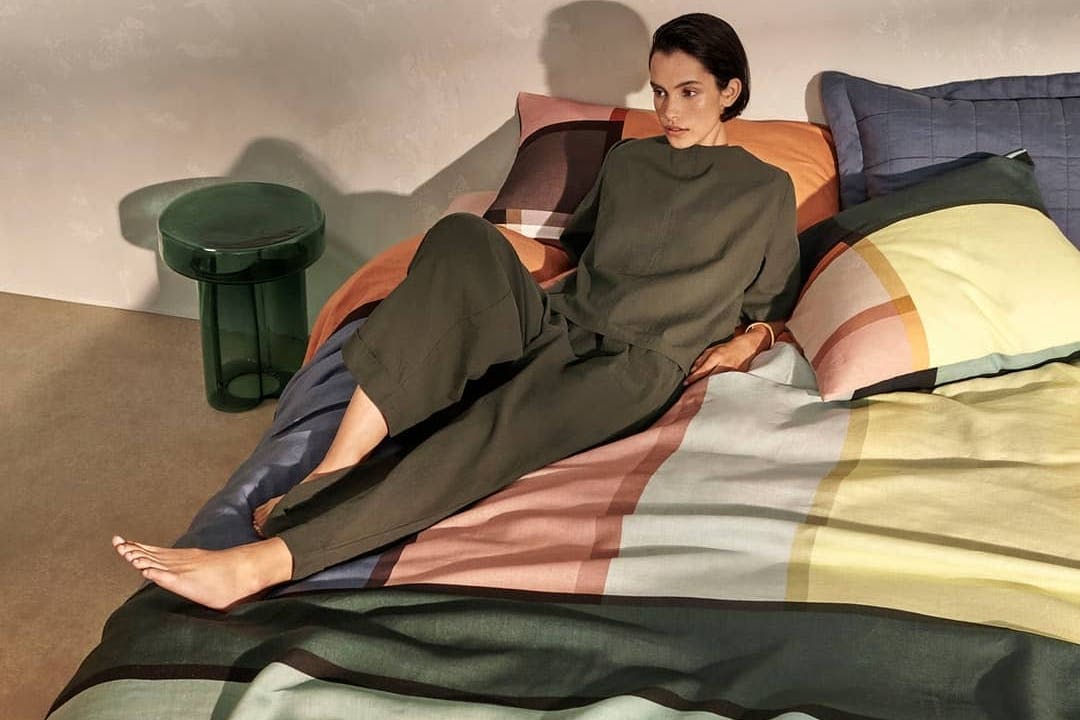 A woman lays upon a bed with a multi-coloured bed spread.